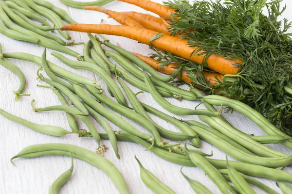 Zanahorias con hojas verdes y frijoles sobre un fondo blanco — Foto de Stock