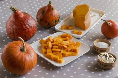 Kabak çorbası yapmak için ürünlerin hazırlanması. Masada kabak, tohum, tuz var. Kesme tahtasında dilimlenmiş balkabağı. Gri polka nokta masa örtüsü