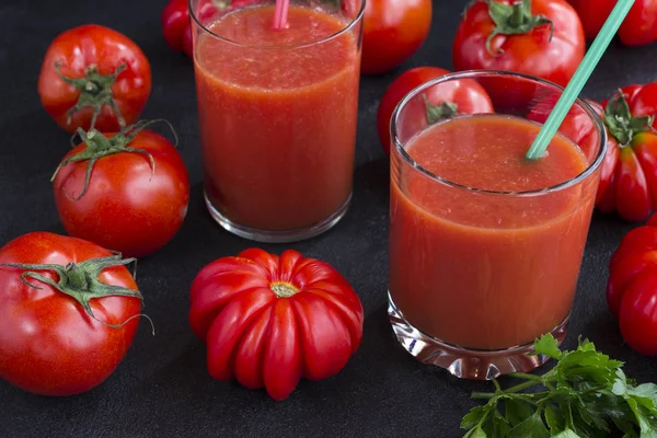 Zwei Gläser Tomatensaft zwischen Tomaten auf schwarzem Hintergrund — Stockfoto