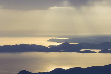 Denizüzerinde gün batımı, dağların yamaçlarında ağaçlar, bulutlar da gökyüzü