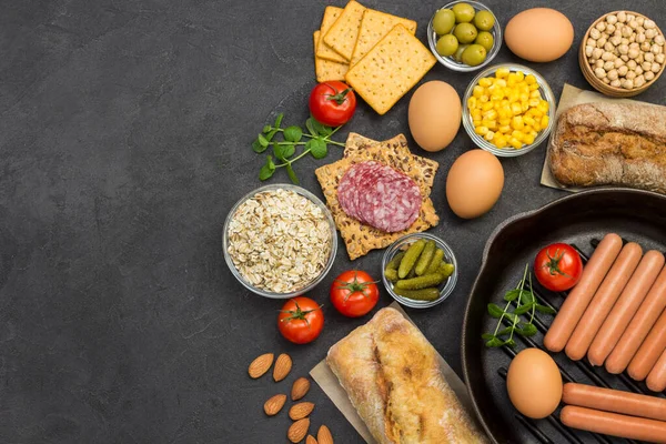 Sausages in pan. Cheese, vegetables, cookies cereal: ingredients for  continental breakfast. Black background. Balanced diet food. Flat lay. Copy space