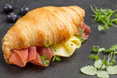 Jamon ve peynirli kruvasan. Yeşiller masada. Siyah arkaplan