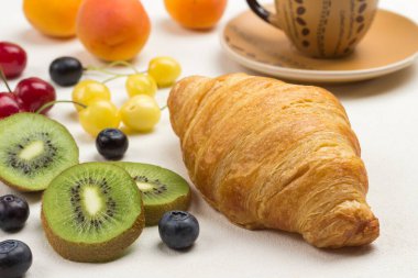 Kivi meyvesi ve yaban mersini, kruvasan, beyaz arka planda kahve fincanı. Üst görünüm