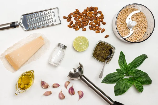 Pesto sauce. Cutter with pine nut, whisk, grater, pesto bowl, basil leaves, parmesan, garlic, lemon. Flat lay. White background