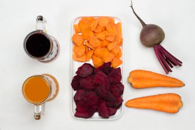 Beyaz tabakta dilimlenmiş pancar ve havuç. Pancar ve havuç kökü. İki bardak pancar ve havuç suyu. Beyaz arka plan. Düz yatıyordu