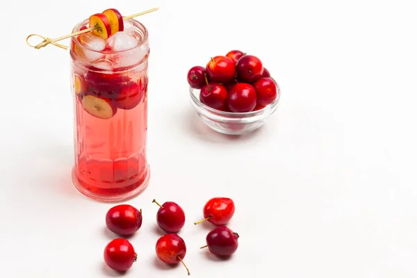 stock image Homemade refreshing summer apple drink with ice in glass. Sliced apples on stick. Small red apples on table and in glass cup. White background. Top view