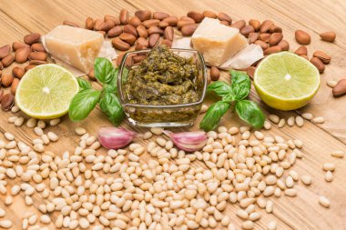 Ev yapımı pesto için malzemeler. Parmesan peyniri, cam bardakta pesto sosu. Limon, fesleğen ve yağ. Sarımsak ve çam fıstığı. Üst Manzara. Hafif ahşap arkaplan