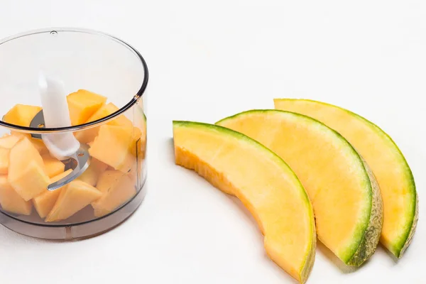 Sliced melon on table. Melon cut into pieces in blender jar. White background. Top view
