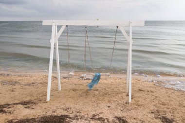 Deniz kenarında salıncakta sallanan mavi eşarp. Kumdaki yosunlar. Sudaki denizanası