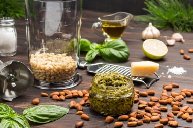 Pesto sosu. Çam fıstığıyla karıştırma kavanozu. Parmesanla çırpın ve rendeleyin. Kasede pesto, fesleğen yaprağı, sarımsak ve limon. Karanlık ahşap arka plan. Üst görünüm