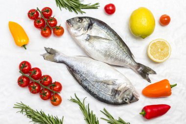Sebzeli taze dorado balığı. Kırmızı domates, renkli biber, yeşil biberiye, beyaz arka planda limon. Düz yatıyordu