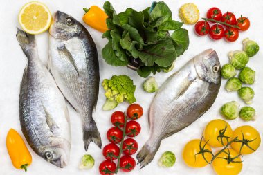 Sebzeli ve yeşillikli taze dorado balığı. Kırmızı domates, renkli biber ve yeşil biberiye, limon ve Brüksel lahanası. Beyaz arka plan. Düz yatıyordu