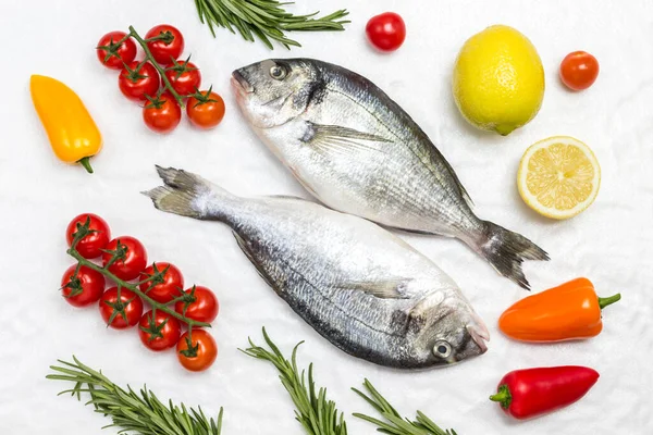 Sebzeli taze dorado balığı. Kırmızı domates, renkli biber, yeşil biberiye, beyaz arka planda limon. Düz yatıyordu