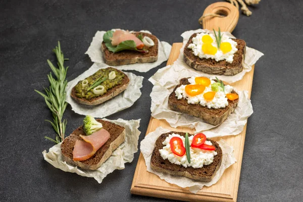 Variety of sandwiches for breakfast and appetizers on board and table. Black background. Top view