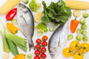 Sebzeli taze dorado balığı. Kırmızı domates, renkli biber, yeşil biberiye, beyaz arka planda limon. Düz yatıyordu