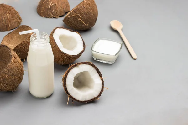 Half a coconut, bottle of coconut milk with straw. Coconut yogurt in bowl. Coconut shells. Grey background. Top view. Copy space