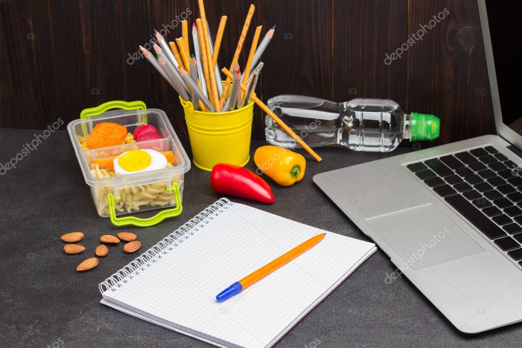 Yellow pen on notebook with springs. Bottle of water. Launch Box. Bucket of pencils and Laptop. Black background
