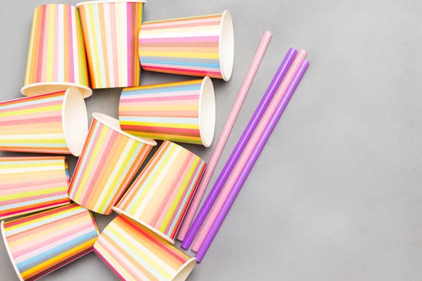 Colorful paper cups and colorful plastic straws for drinks. Grey background. Flat lay. Reuse, environmental concept. Copy space
