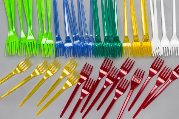 Colorful plastic forks on gray background. Disposable plastic tableware. Plastic processing problem. Ecology environmental care. Flat lay. Grey background