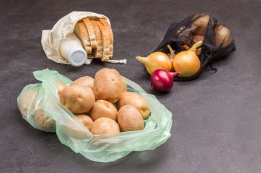 Patatesler plastik torbada. Keten torbada ekmek ve süt. Tekrar kullanılabilir siyah torbada soğanlar. Masada soğan ve sarımsak. Plastik ve organik poşetler arasında seçim yapmak. Eko konsepti. Siyah arka plan. Üst görünüm