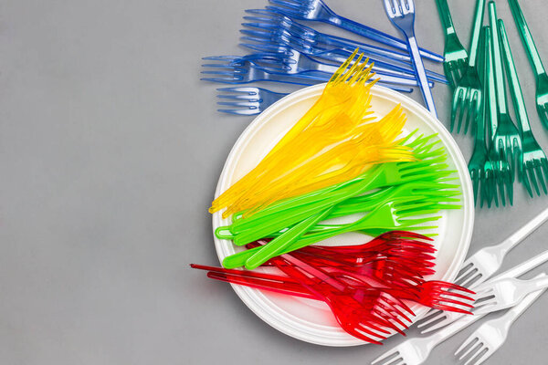 Colorful plastic forks on white plate. Disposable plastic tableware.  Ecology environmental care. Flat lay. Grey background. Copy space