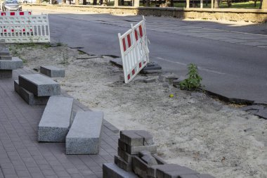 Road repair. Granite curbstone and road bricks at the repair site. Warning barrier on the road.