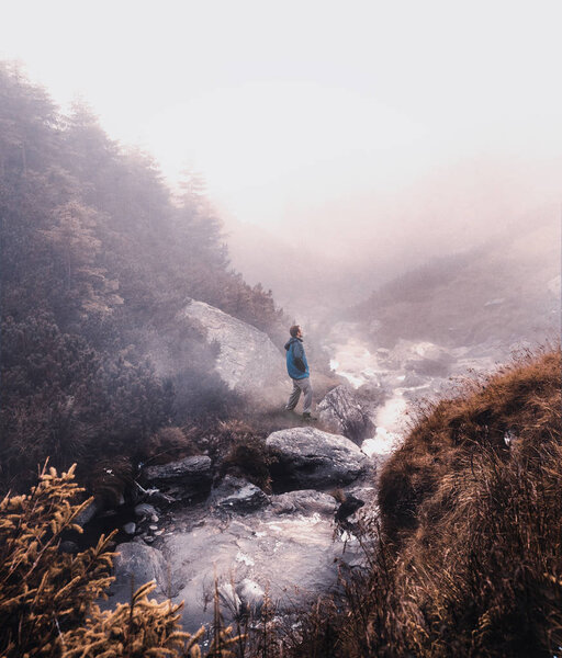Man standing near a mountain river in a foggy day.