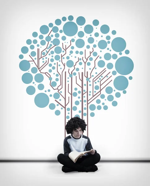 Молодой Человек Читает Книгу Перед Белой Стеной Нарисованной Деревом Плате — стоковое фото