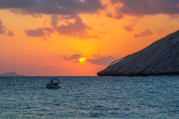 Odak dışında saman şemsiye ile plaj ve deniz üzerinde turuncu ışıklar ile Güzel Sunrise. Gün doğumunda denizde tekne