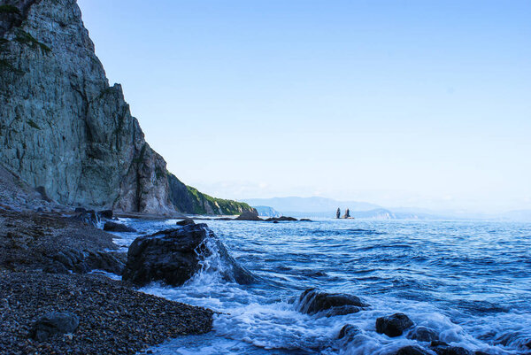 Скалистый берег моря зажат нависающими камнями. Волна
