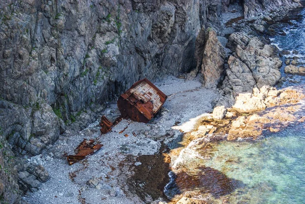 Una vecchia nave naufragata si trova sulla riva ai piedi di un roc — Foto Stock