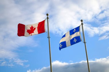 Rüzgârla birlikte mavi gökyüzü içinde çırpınan Quebec ve Kanada bayrakları