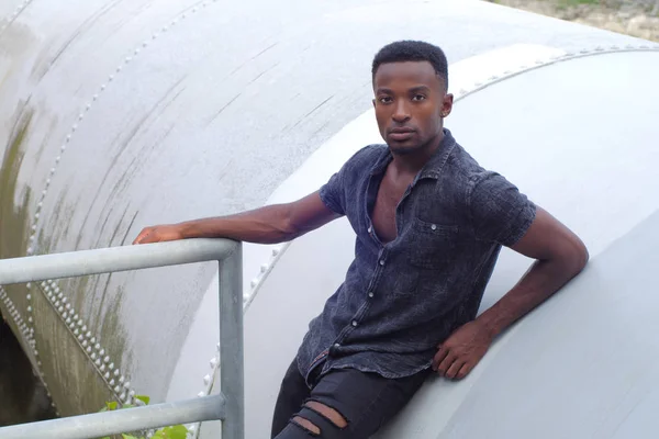 Fiatal afrikai férfi underground portré szakadt farmer ipari háttér — Stock Fotó