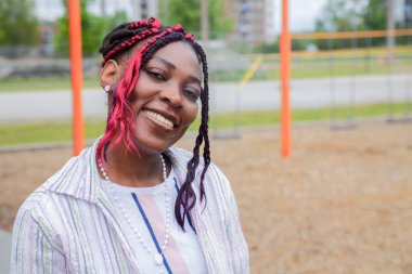 Bir çocuk parkında, gülümseyen Afrikalı Amerikalı anaokulu öğretmeni çocukları denetliyor. Erken eğitim, okul ortamı, çocuk bakımı, öğrenme ve çeşitlilik tasvirleri için ideal.