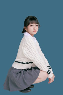 Mavi arka planda tecrit edilmiş, lise üniformalı genç bir Asyalı kız öğrencinin portresi. Sevimli ve mutlu Asyalı ergen. Okula ya da kampüs hayatı konseptine.