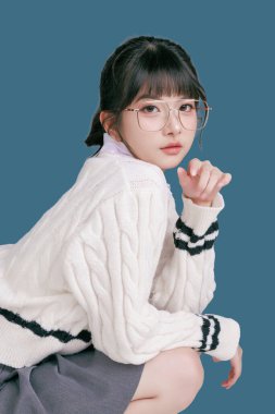 Mavi arka planda tecrit edilmiş, lise üniformalı genç bir Asyalı kız öğrencinin portresi. Sevimli ve mutlu Asyalı ergen. Okula ya da kampüs hayatı konseptine.