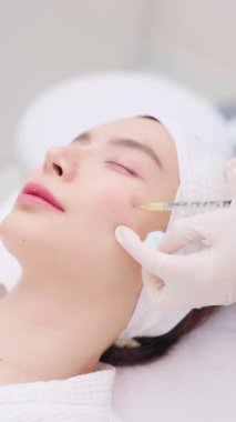 Genç bir Asyalı kadının botoks ya da bir profesyonelden yüzüne deri doldurucu iğnesi alırken çekilmiş yakın plan fotoğrafı. Güzellik klinikleri, dermatoloji ve yaşlanma karşıtı tedaviler kavramı.