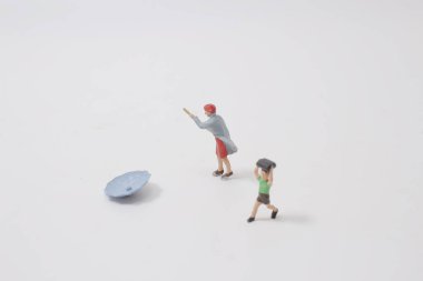 Mini figür şemsiyeyle yağmurun altında yürüyor.,