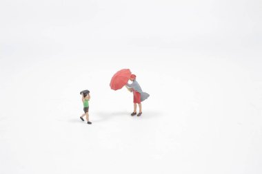 Mini figür şemsiyeyle yağmurun altında yürüyor.,