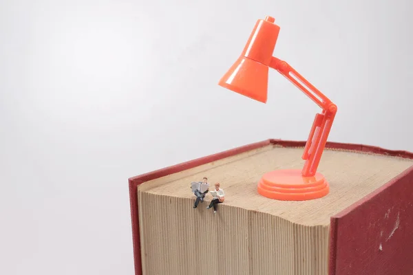 mini people sitting on book with lamp idea using as background