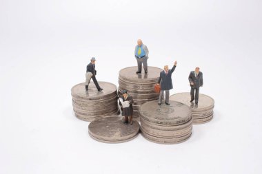 Bir iş adamı minyatür insan figürü gümüş para yığınının üstünde duruyor.