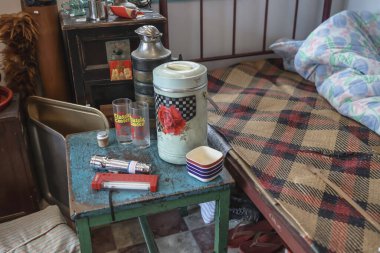 Desenli yatak ve yorganın yanında dekoratif eşyaların olduğu eski bir tablo gösteriliyor.