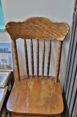 Ayrıntılı ahşap bir sandalyede elle oyulmuş süslemeli bir sırt çantası bulunur.