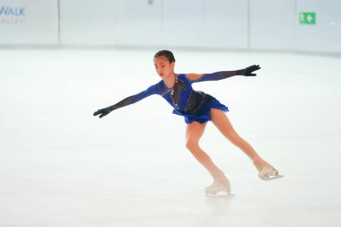 Mavi elbiseli yetenekli artistik patinajcı zarif bir şekilde karmaşık bir duruş sergiliyor.