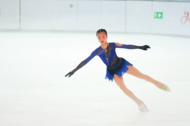 Mavi elbiseli yetenekli artistik patinajcı zarif bir şekilde karmaşık bir duruş sergiliyor.