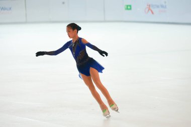 Mavi elbiseli yetenekli artistik patinajcı zarif bir şekilde karmaşık bir duruş sergiliyor.