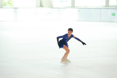 Mavi elbiseli yetenekli artistik patinajcı zarif bir şekilde karmaşık bir duruş sergiliyor.