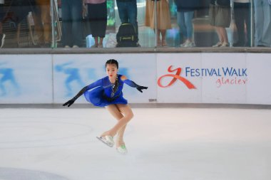 Mavi elbiseli yetenekli artistik patinajcı zarif bir şekilde karmaşık bir duruş sergiliyor.