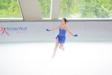 Mavi elbiseli yetenekli artistik patinajcı zarif bir şekilde karmaşık bir duruş sergiliyor.