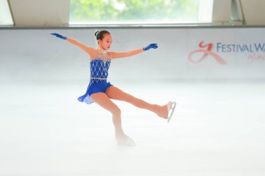 Mavi elbiseli yetenekli artistik patinajcı zarif bir şekilde karmaşık bir duruş sergiliyor.